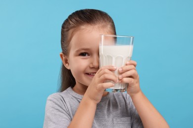 Photo of Cute girl with glass of fresh milk on light blue background
