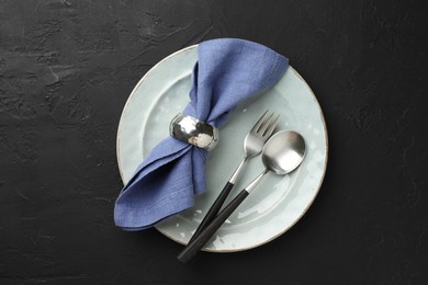 Photo of Stylish setting with cutlery, napkin and plate on dark textured table, top view