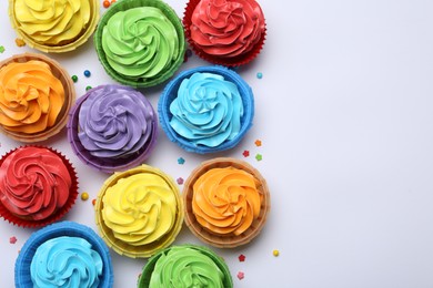 Many tasty cupcakes with bright cream and sprinkles on white background, flat lay. Space for text