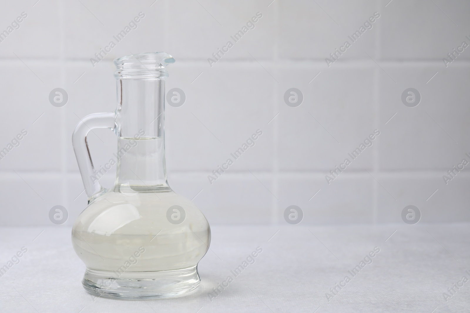 Photo of Vinegar in glass jug on light table, space for text