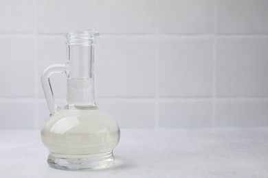 Vinegar in glass jug on light table, space for text