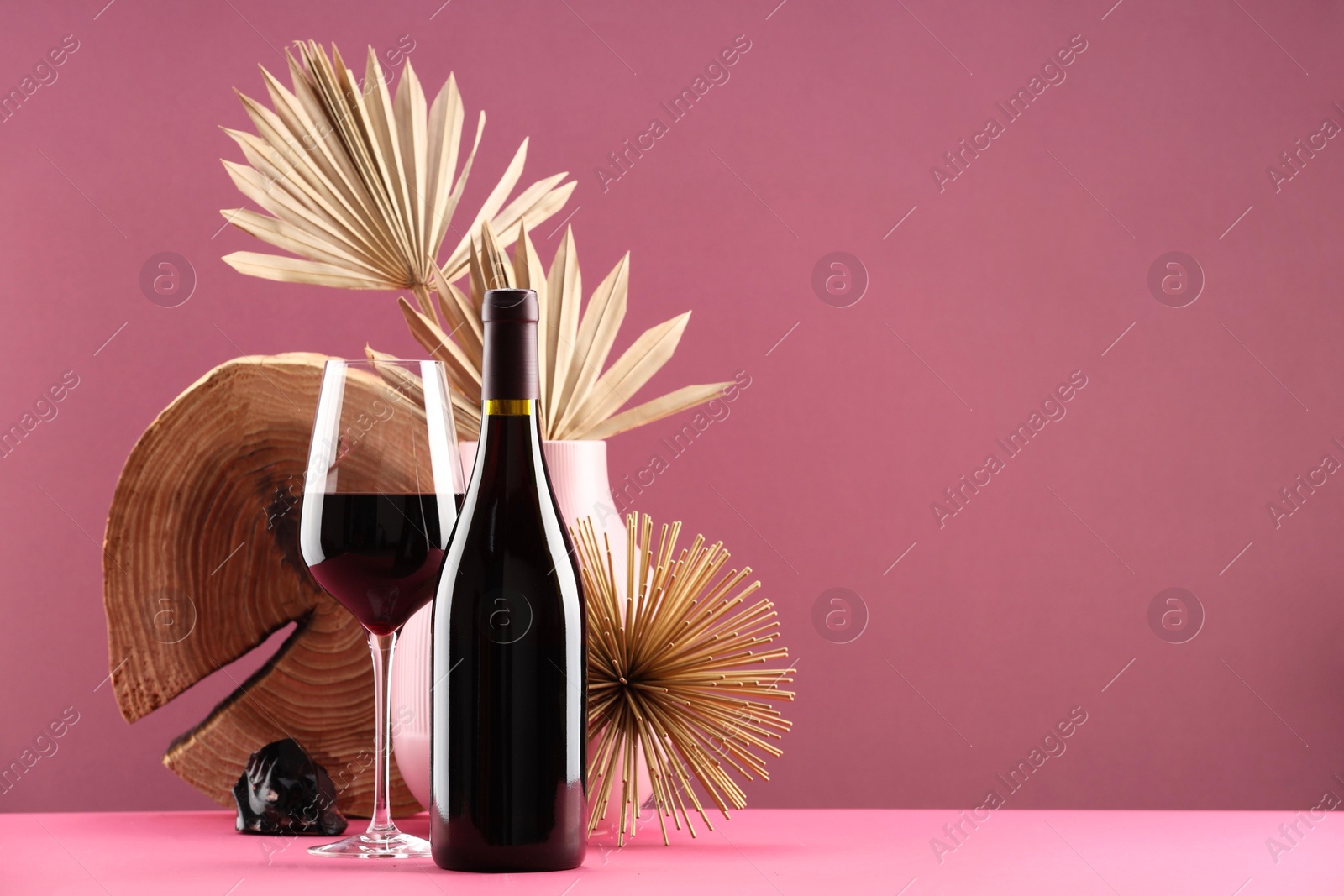 Photo of Stylish presentation of delicious red wine in bottle and glass on pink background. Space for text