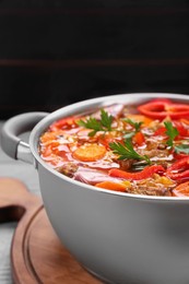 Saucepan of delicious vegetable soup with meat and ingredients on grey wooden table, closeup