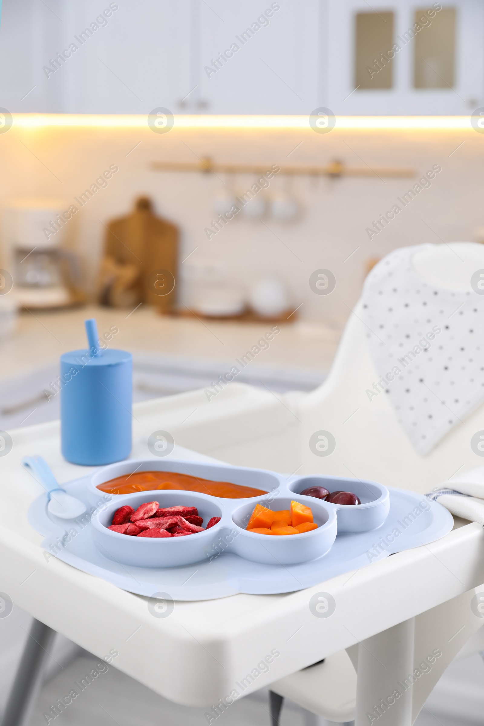 Photo of High chair with food in baby tableware on white tray indoors