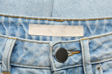Photo of Blank clothing label on light blue jeans, top view