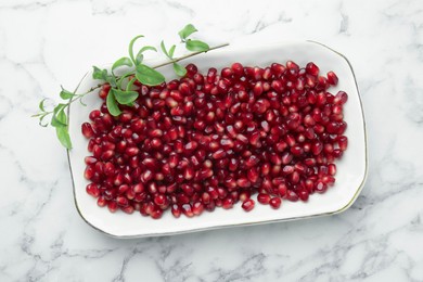 Photo of Ripe juicy pomegranate grains and green leaves on white marble table, top view