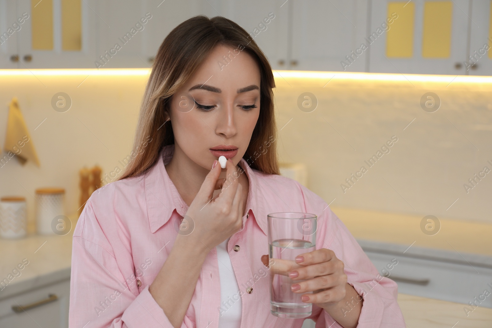 Photo of Young woman taking abortion pill in kitchen