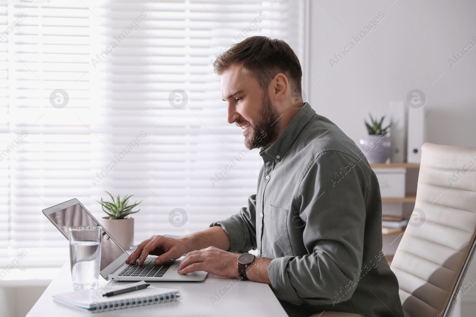 Photo of Young man working on laptop at table in office