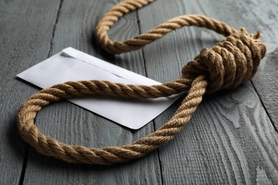 Photo of Rope noose and blank envelope on grey wooden table, closeup