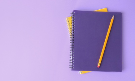 Photo of Notebooks with pencil on lilac background, top view. Space for text