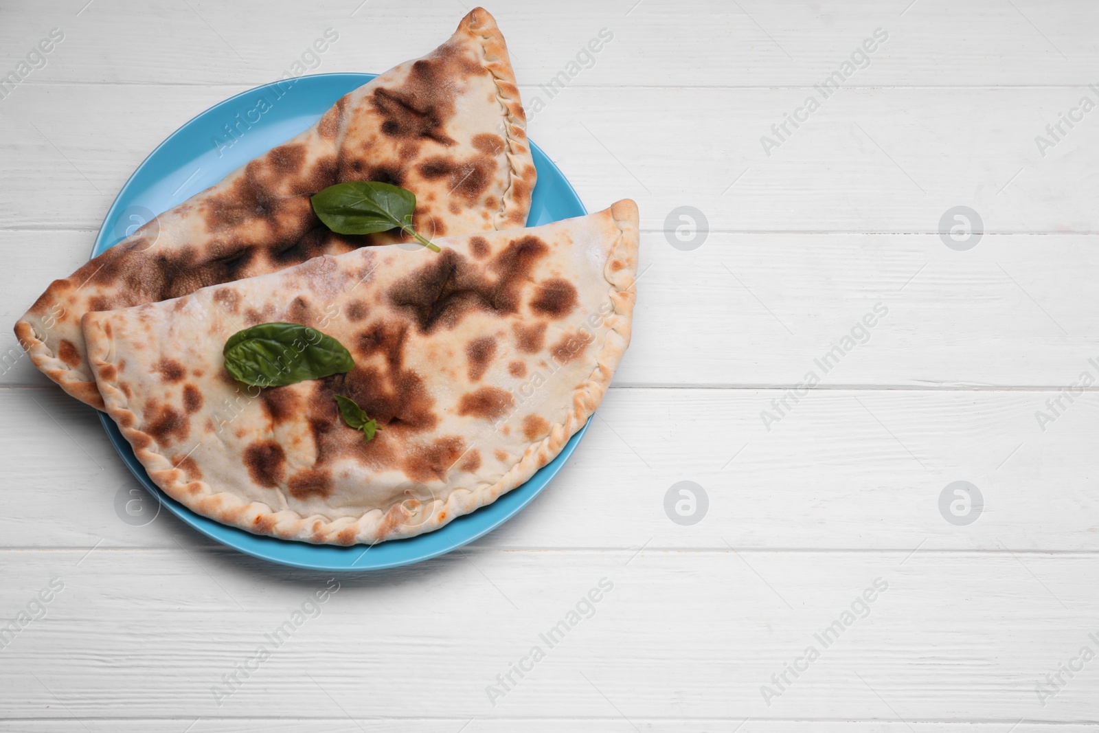 Photo of Plate with delicious calzones on white wooden table, top view. Space for text