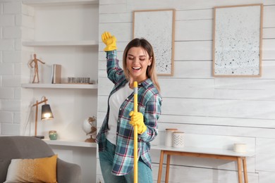 Photo of Woman with mop singing while cleaning at home