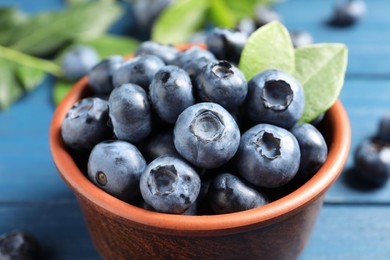 Tasty fresh blueberries in bowl on blue wooden table, closeup
