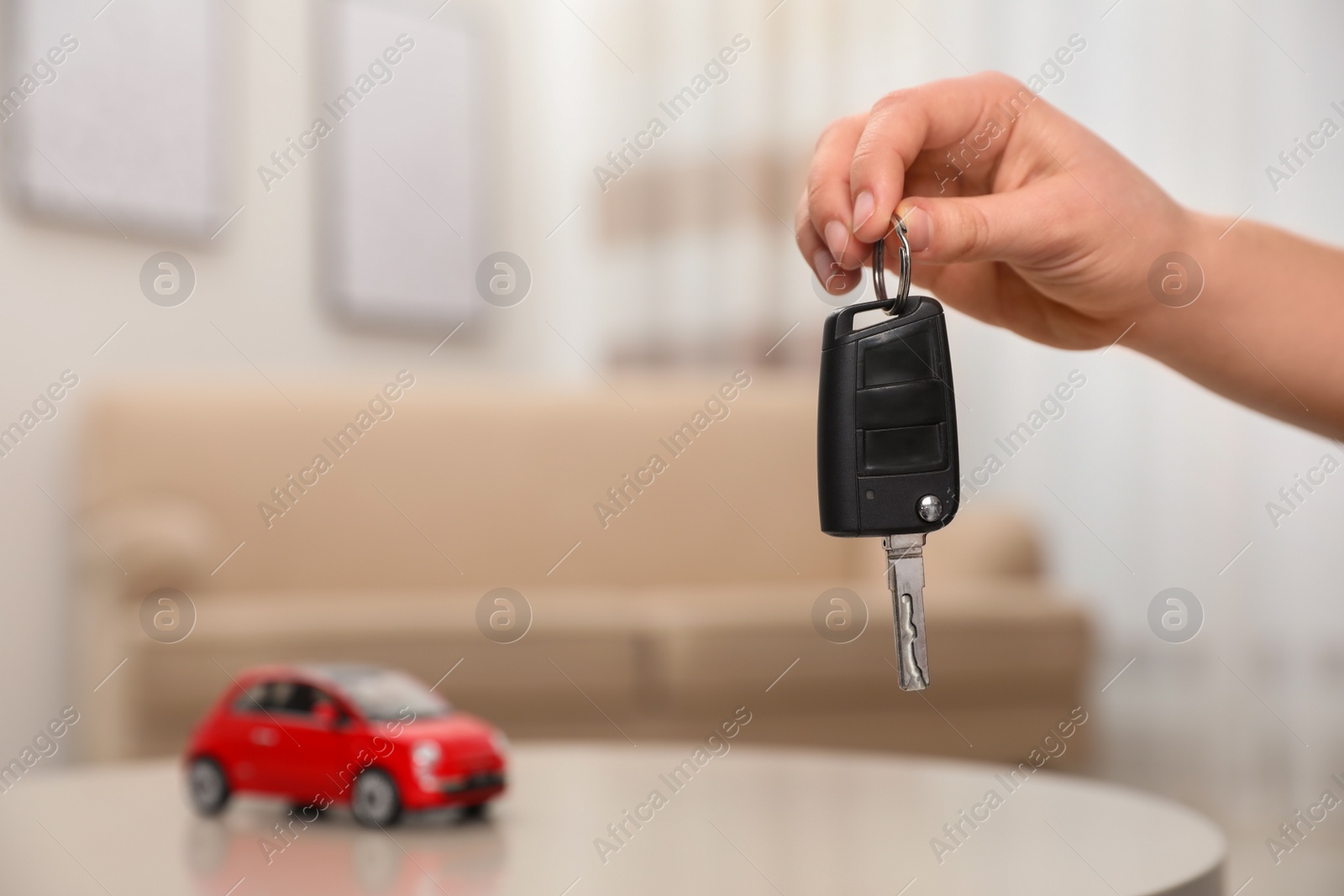 Photo of Man holding key near table with miniature automobile model indoors, closeup. Car buying