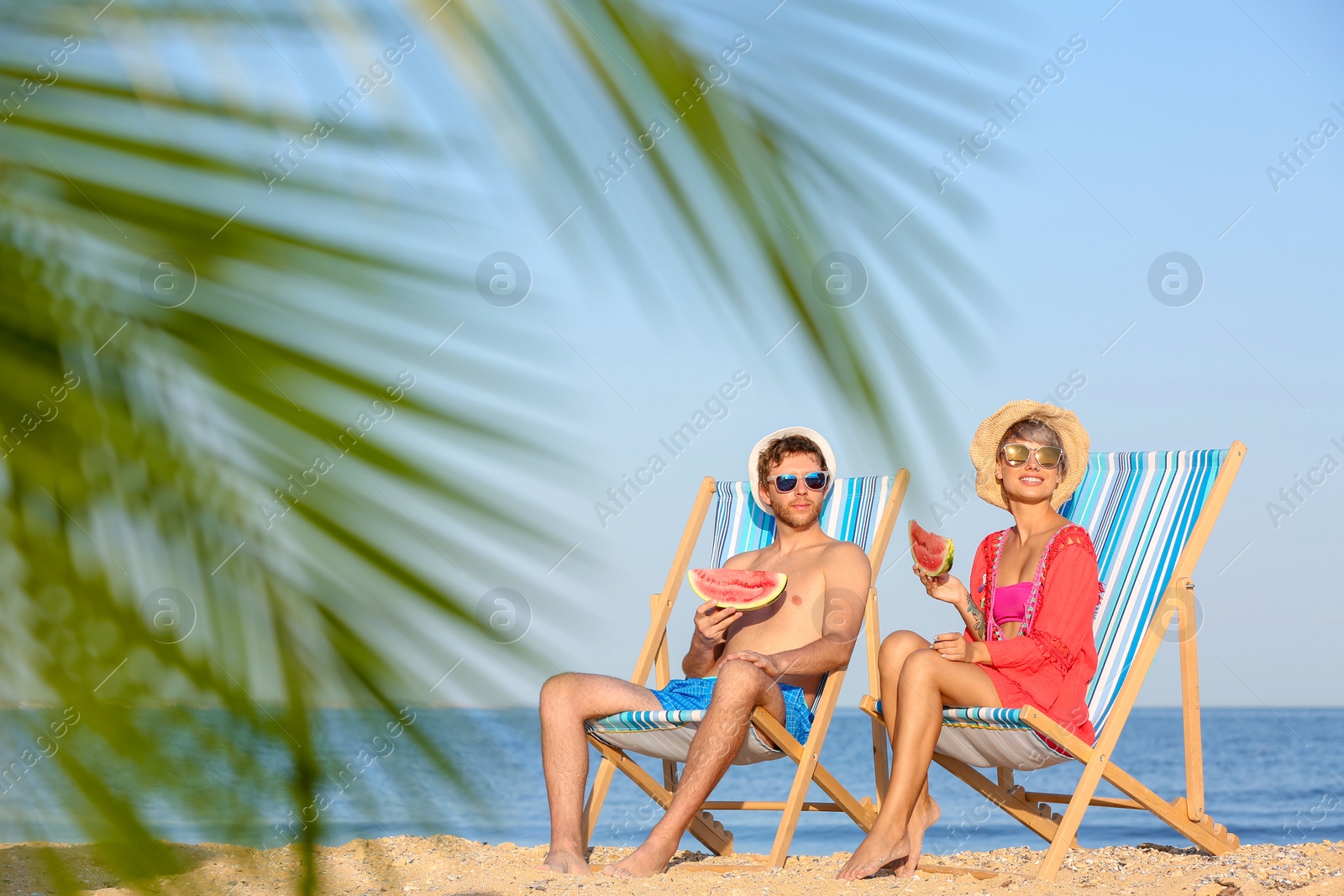 Photo of Young couple with watermelon slices in beach chairs at seacoast