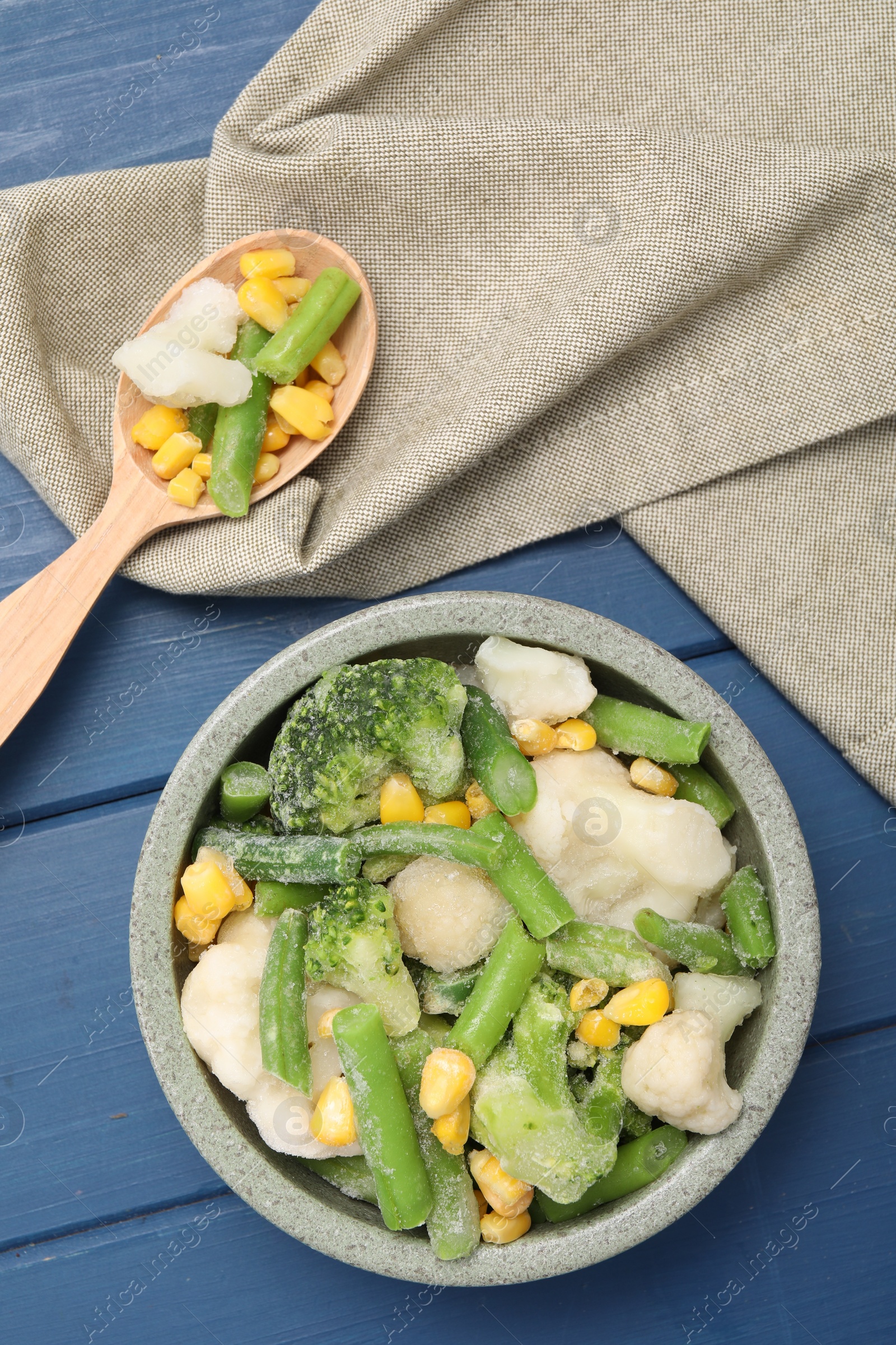 Photo of Mix of different frozen vegetables in bowl on blue wooden table, top view