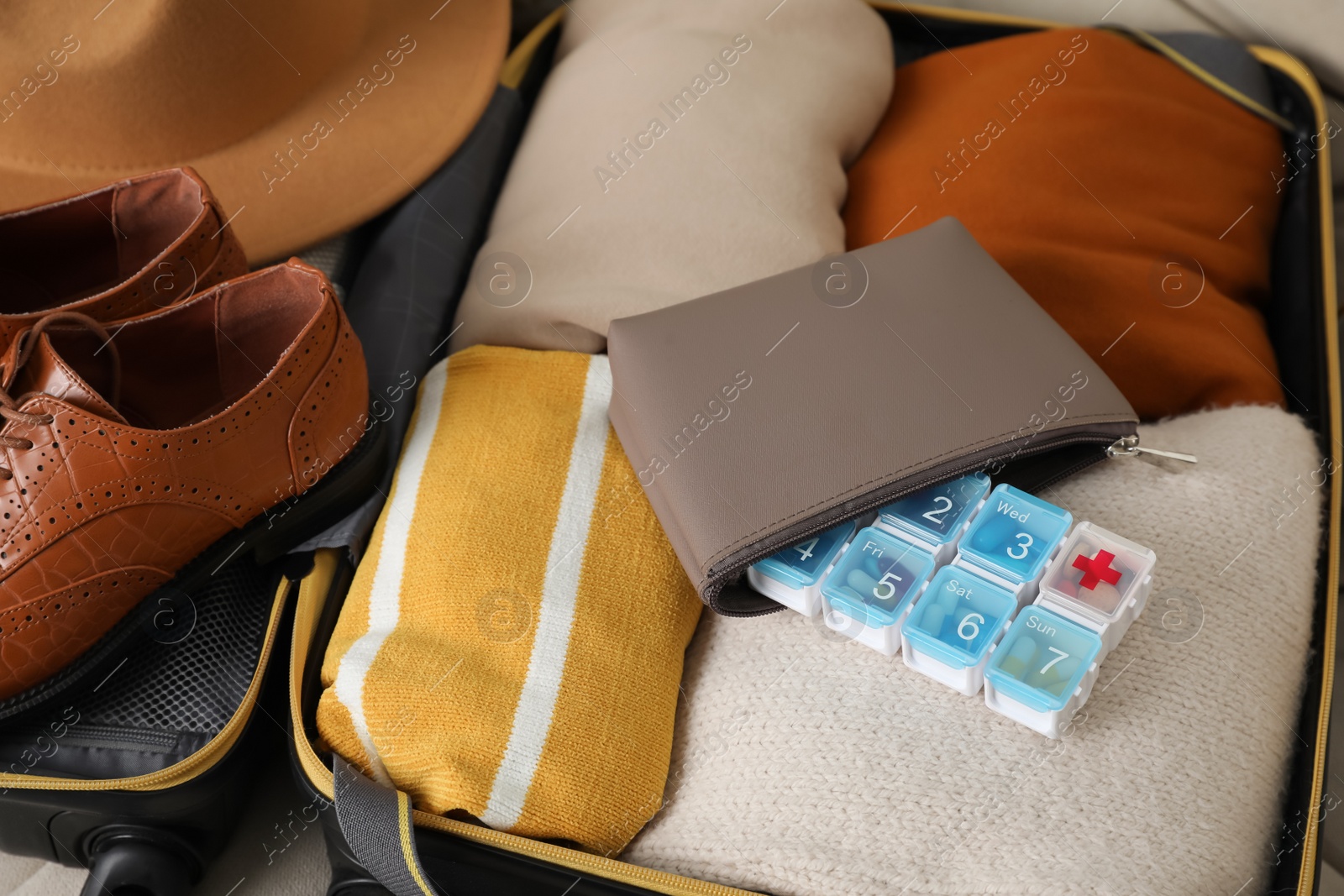 Photo of Open suitcase with packed clothes, accessories and pill box, closeup