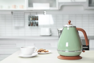 Photo of Modern electric kettle, cup and cookies on wooden table in kitchen