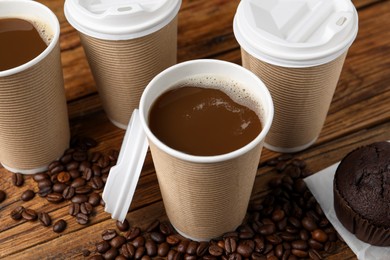 Photo of Coffee to go. Paper cups with tasty drink and beans on wooden table, closeup