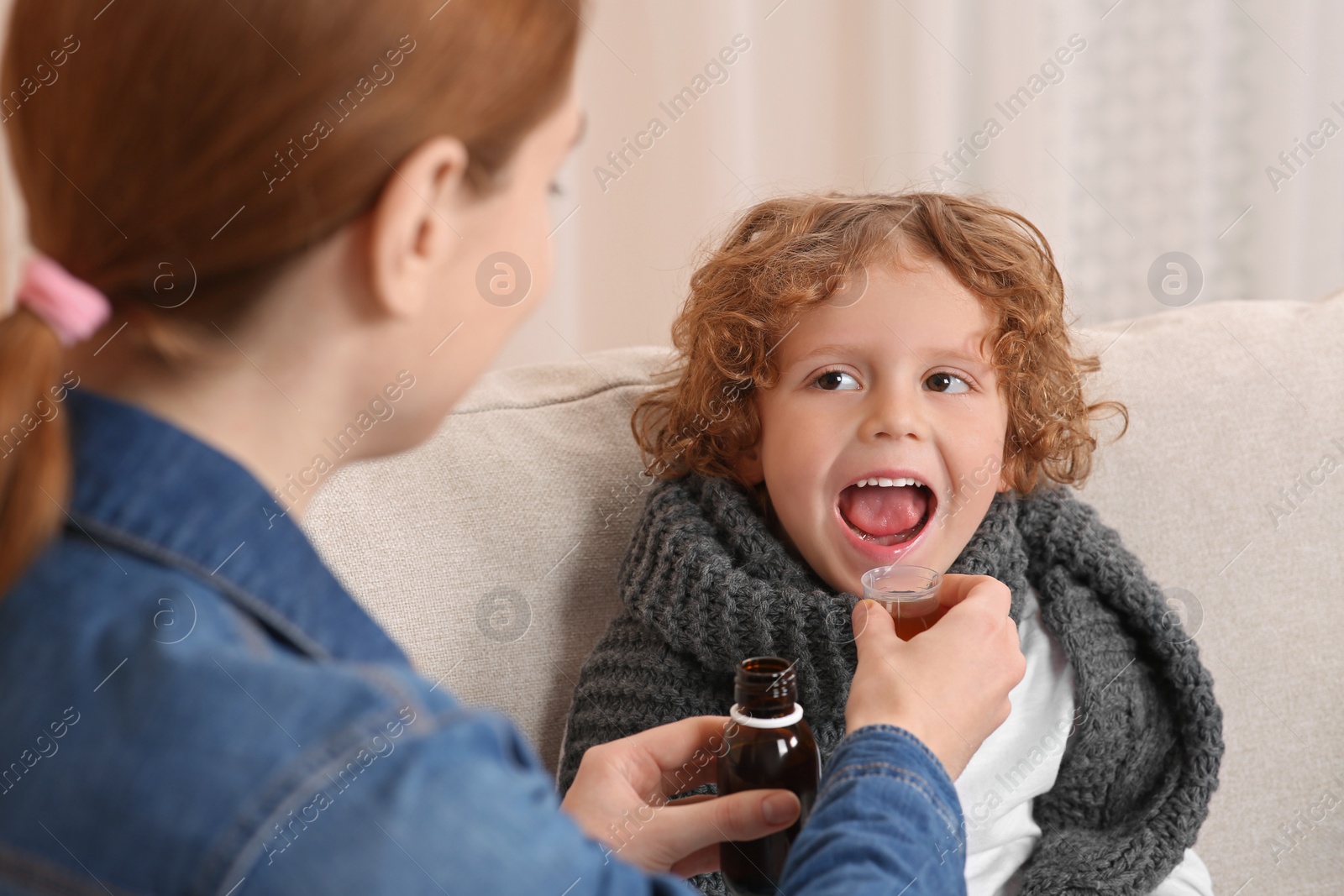 Photo of Mother giving cough syrup to her son on sofa