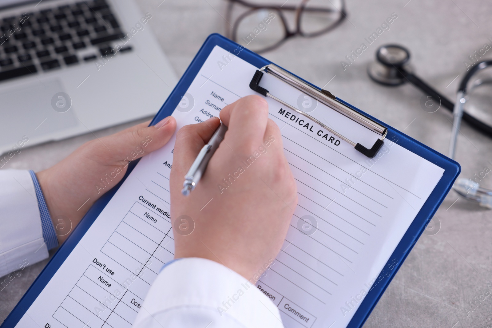 Photo of Doctor filling out patient's medical card at table in clinic, closeup