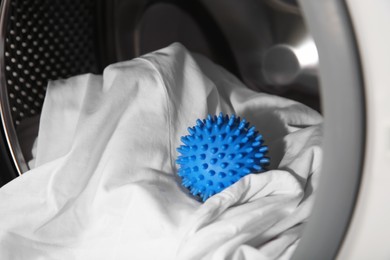 Photo of Blue dryer ball and clothes in washing machine drum, closeup