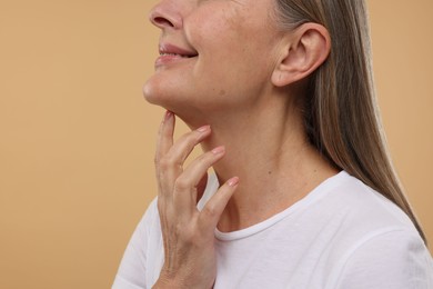 Mature woman with healthy skin on beige background, closeup