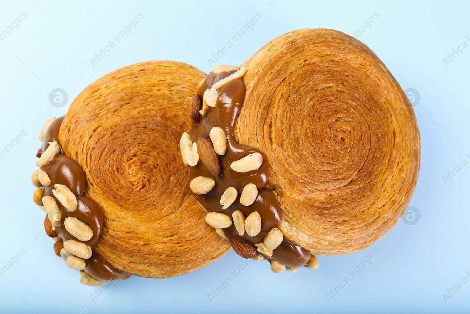 Photo of Supreme croissants with chocolate paste and nuts on light blue background, above view. Tasty puff pastry