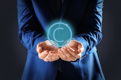 Man holding virtual icon of copyright symbol on dark background, closeup