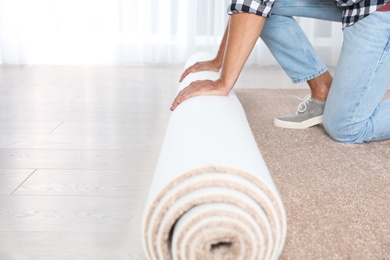 Photo of Man rolling out new carpet flooring indoors, closeup. Space for text