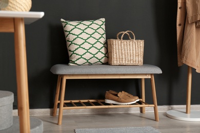 Photo of Bench with pillow and bag at black wall. Interior design