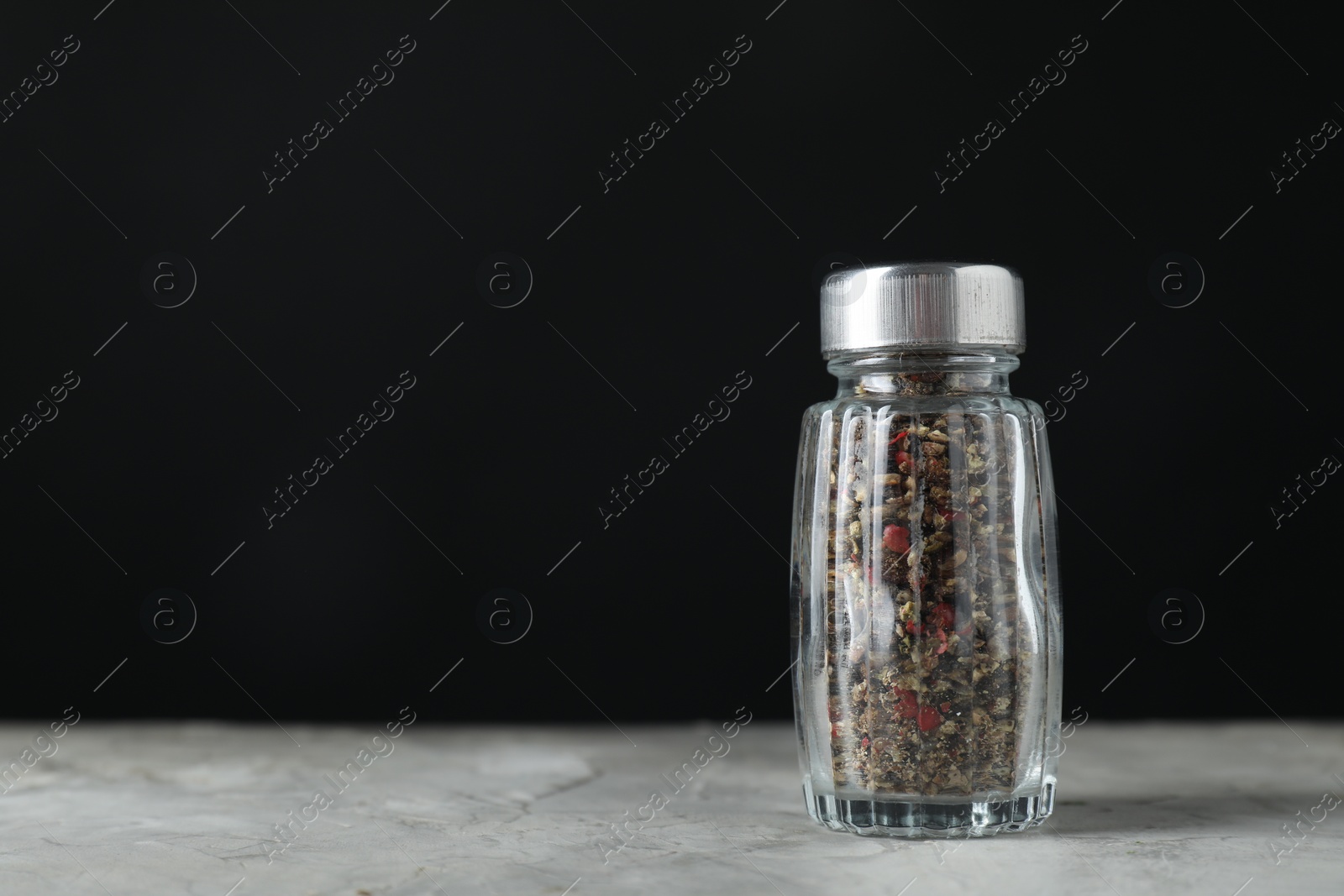 Photo of Pepper shaker on light textured table against black background. Space for text