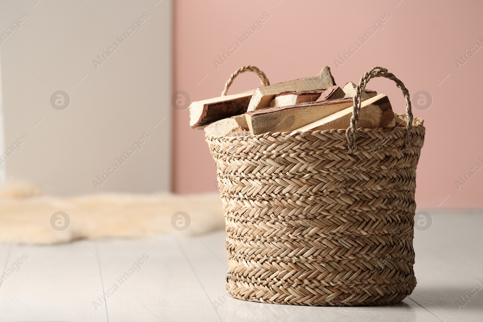 Photo of Wicker basket with cut firewood on white floor indoors