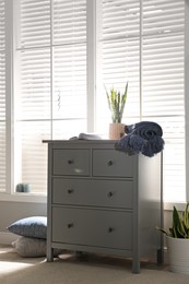 Grey chest of drawers near window in stylish room interior