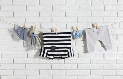 Photo of Baby clothes hanging on washing line near white brick wall