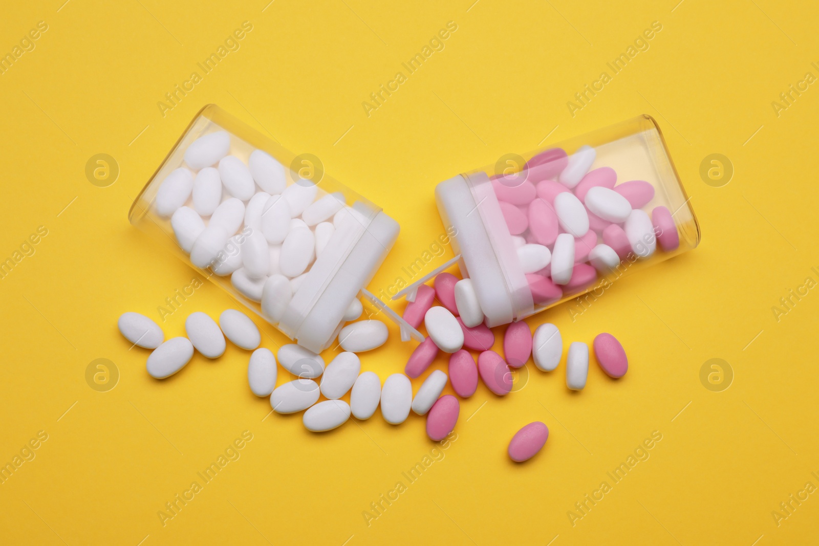 Photo of Containers and different dragee candies on yellow background, flat lay