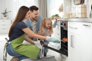 Photo of Woman and her family taking out tray with baked buns from oven in kitchen