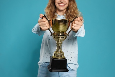 Photo of Young woman with gold trophy cup on blue background, closeup