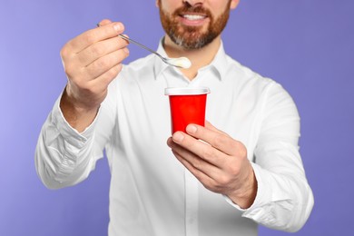 Photo of Man with delicious yogurt on violet background, closeup