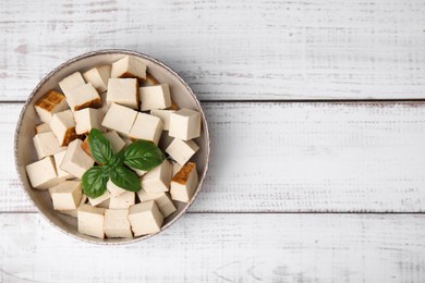 Photo of Bowl with delicious smoked tofu and basil on white wooden table, top view