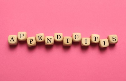 Photo of Word Appendicitis made of wooden cubes with letters on pink background, top view