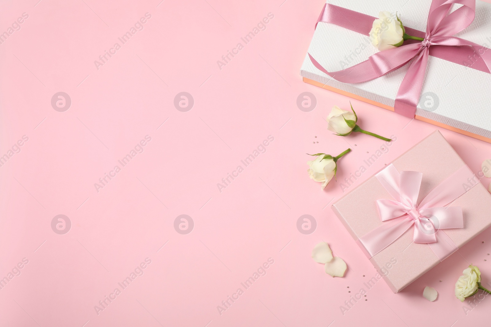 Photo of Elegant gift boxes and beautiful flowers on pink background, flat lay. Space for text