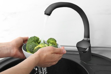 Photo of Woman washing bowl of fresh green broccoli in kitchen sink, closeup view