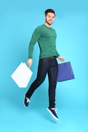 Full length portrait of young man jumping with paper bags on blue background