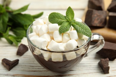 Glass cup of delicious hot chocolate with marshmallows and fresh mint on white wooden table, closeup