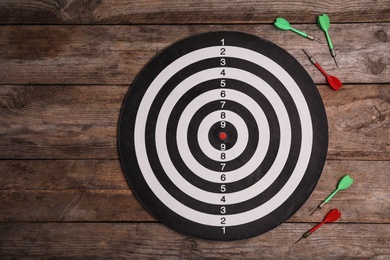 Dart board with color arrows on wooden background, top view. Space for text