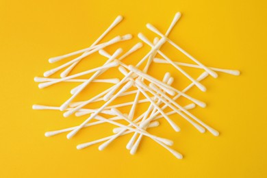 Many clean cotton buds on yellow background, flat lay