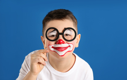 Photo of Preteen boy with clown makeup and party glasses on blue background. April fool's day