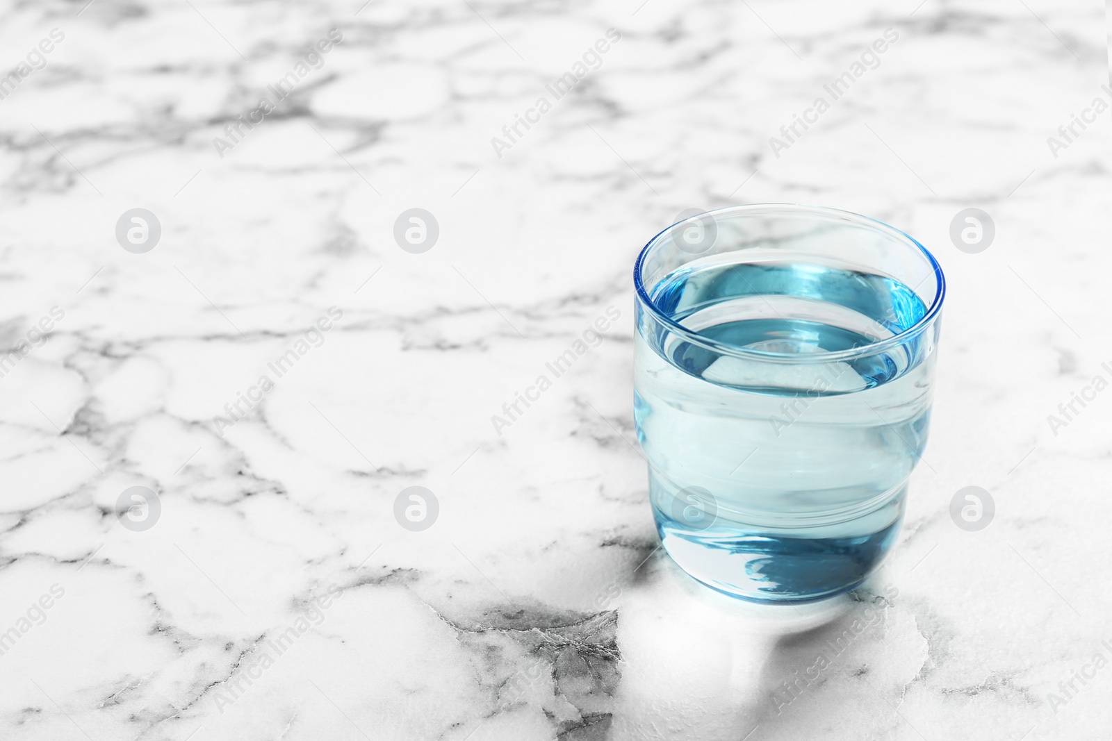 Photo of Glass with fresh water on marble table. Space for text