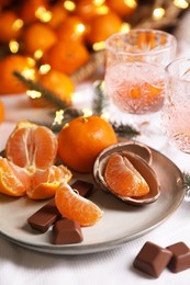 Delicious ripe tangerines, chocolates, festive lights and glasses of wine on white bedsheet